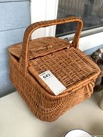 Front and top view of wicker picnic basket showing handle and lid.
