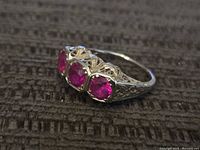 Side view of filigree 18k white gold ring showing three pink stones and detailed gallery