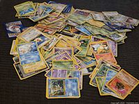Large pile of assorted Pokémon cards spread on dark fabric surface