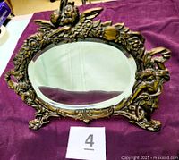 Front view showing oval beveled mirror, cherub and floral cast frame, footed base