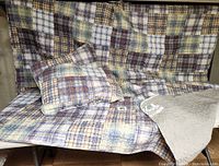 Full view of plaid quilted bedspread draped on surface with matching pillows