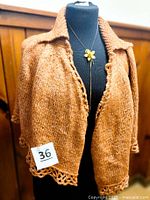 Front view of pumpkin knit capelet on mannequin with necklace displayed