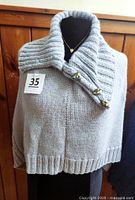 Front view of gray knitted cape on mannequin with buttons and collar visible