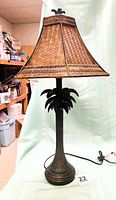 Full view of lamp showing base, palm tree stem, shade and cord