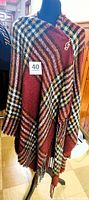 Full view of plaid wool cape on mannequin with fringe and pinned number tag