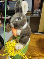 Brown plush bunny in green pot with yellow grass, holding carrot