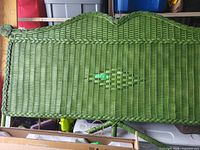 Front view of green wicker headboard showing overall weave and braided trim