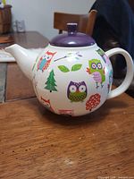 Left side view of ceramic teapot showing owl graphics and purple lid