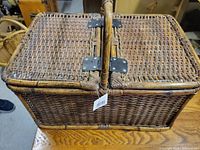 Full view of rectangular wicker picnic basket showing woven exterior, split hinged lid, central carry handle and attached tag