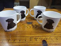 Four white mugs with Labrador graphic displayed on wooden surface