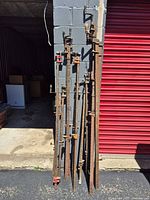 Group of 14 long pipe clamps leaning against wall