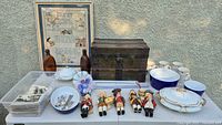 Overall view of all items on table including trunk, dolls, tableware, bottles, flatware