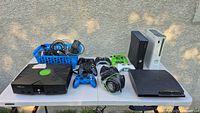 Overview of four consoles on table with controllers, headset, cables basket