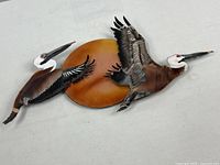 Full view of enameled metal wall art showing two pelicans and sun