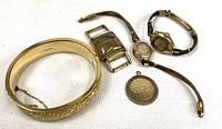 All five gold-filled items laid out: hinged bangle, two wristwatches, rectangular component, round pendant