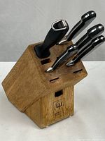 Angled view of oak knife block with four knives and honing steel inserted, Wüsthof logo visible