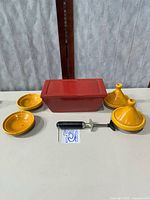 Group shot of red loaf pan, yellow Moroccan dishes and lids, wine openers