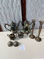 Group view of coffee pot, teapot, creamer with detached lid piece, sugar bowl without lid, and two candlesticks