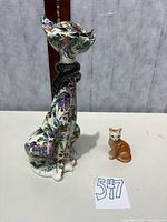 Large floral porcelain cat and small tan cat figurine side by side