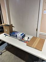 All items on table: boxed shelving unit, cardboard box with rocks, watering wand, garden hose package, slate piece