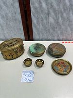 All brass items laid out: cricket box, two round boxes, two candle holders, stack of five plates