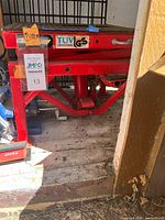 Side view of red Team Hawg scissor lift table showing frame and hydraulic cylinder