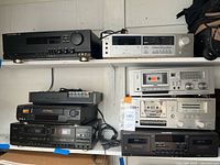 Overview showing black Harman Kardon receiver, silver stereo receiver, small black device, VCR and two cassette decks
