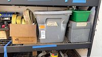 Shelving section with cardboard box of straps, grey plastic tote labelled Safety Ropes, green bin, grey metal case