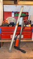 Overall shot of red toolbox on shelf with tire pump leaning against it and tent poles in front