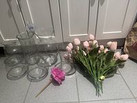 Group of five clear glass vases, bunch of pink tulip stems and single purple rose stem