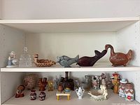 Wide shot of both shelves showing arrangement of figurines, pottery and glass dish