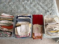 overview of three bins and one stack of assorted linens on bed