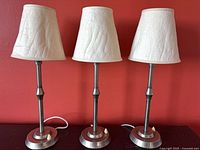 Front view of three matching brushed nickel table lamps with cream shades