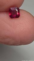 Close-up of ruby held between fingers, showing octagon cut and red colour