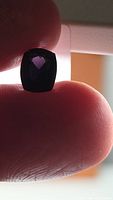 Cushion cut purple spinel held between fingers under backlight