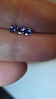 Three cushion cut tanzanite gemstones shown on fingertip
