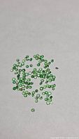 Cluster of small vivid green round gemstones on neutral background