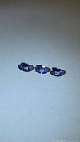Three oval-cut blue-purple gemstones on neutral background