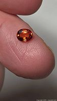 Oval orange sapphire on fingertip showing size and color