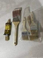 Six paint brushes: one 1.5" in sleeve, one 2.5", four 2" in plastic