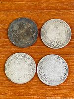Front and back of four worn Canadian 25 cent coins on wooden surface