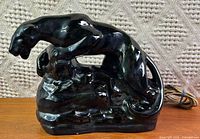 Left profile of glossy black ceramic panther TV lamp showing cord