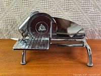 Side profile of entire chrome meat slicer showing blade, carriage and legs