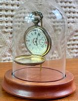 Pocket watch hanging in glass dome on wood base