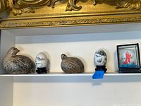 Shelf view showing both ceramic birds, two eggs on stands, empty stand with tape, and glass display box with egg