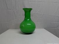 front view of green cased glass vase showing bulbous base, narrow neck, clear handles