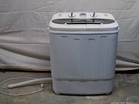 Front view of white twin-tub portable washer dryer with attached drain hose