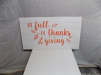 Front of white wood wall sign with orange text and leaves