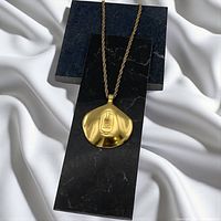 Full view of pendant on dark backdrop, showing shell shape and cartouche motif