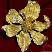 Front view of gold-tone flower brooch on red fabric